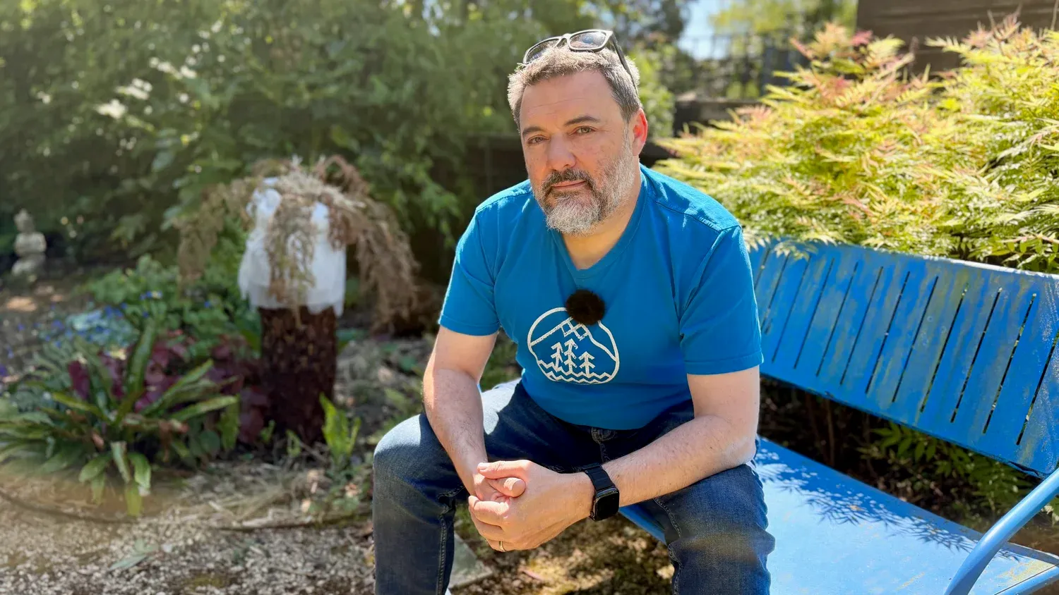 Chris Goor sitting on a blue bench in a garden, talking to camera