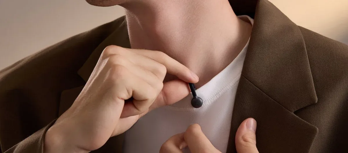 Hands clipping a small lapel microphone to the collar of a brown jacket